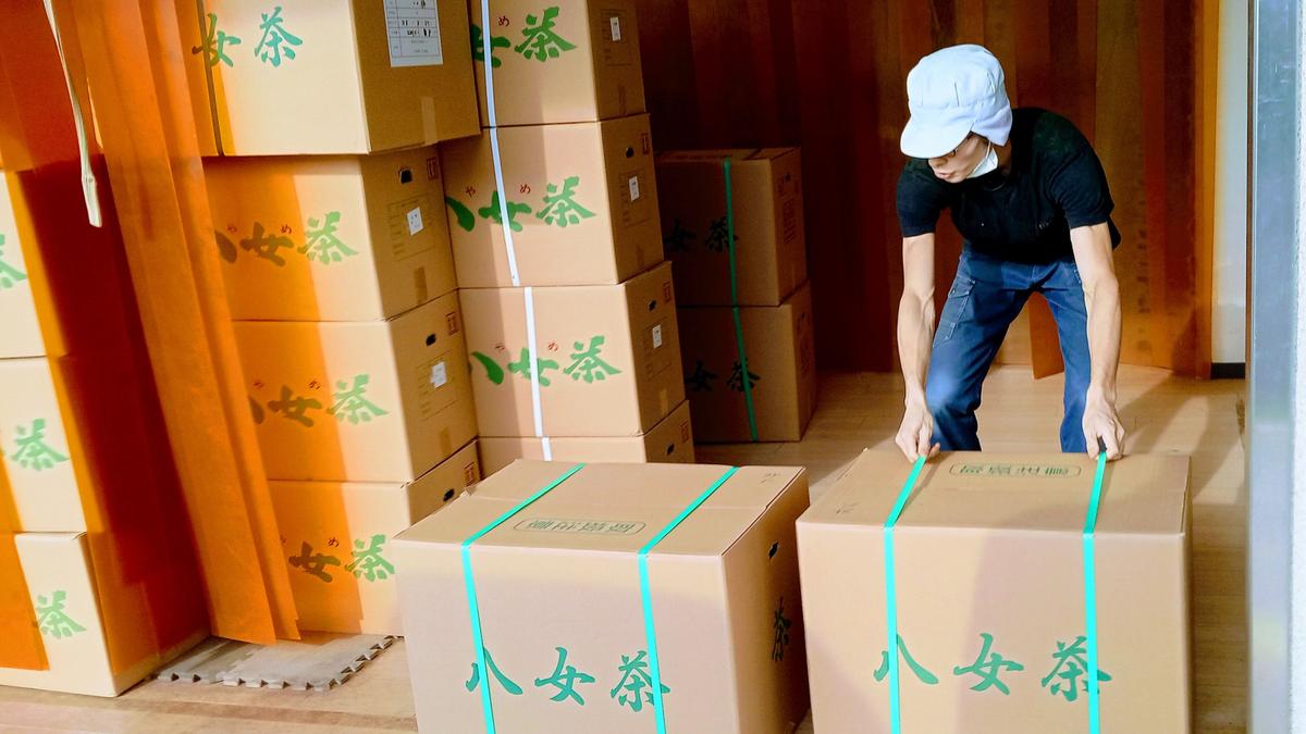 A Yame tea worker arranging large boxes of tea inside a wooden storehouse.