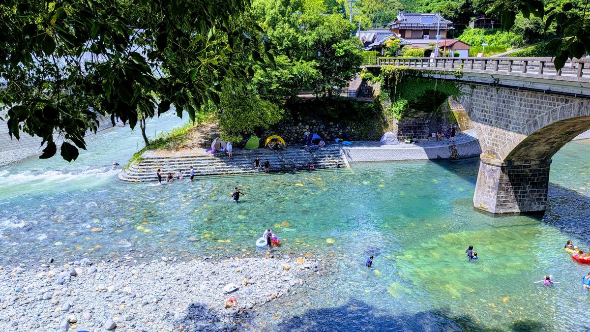 Families swimming in the clear Hoshino River beneath a stone bridge in Jōyō Town, Yame.